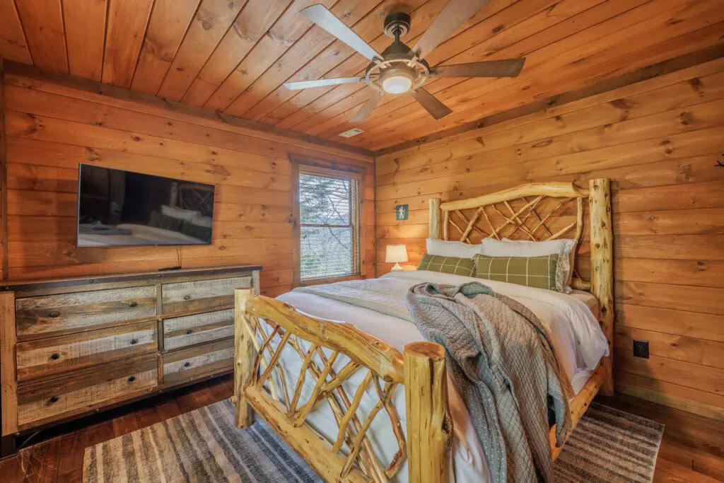 Above the Clouds cabin upstairs bedroom with log twig bed frame and mounted TV in Blue Ridge Georgia