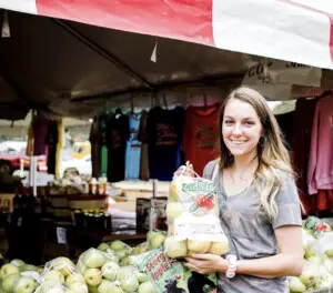 Smiling woman holding a bag of fresh apples at a farm market stand during the Georgia Apple Festival in Ellijay, Georgia.