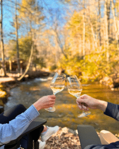 Couple toasting wine glasses by Fightingtown creek at Stone Creek cabin in Blue Ridge, GA