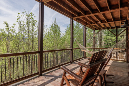 Above the Clouds cabin covered deck with hammock and log Adirondack chairs surrounded by spring foliage in Blue Ridge Georgia
