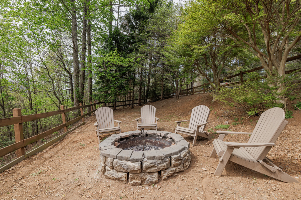 Above the Clouds cabin outdoor stone fire pit with Adirondack chairs surrounded by wooded hillside in Blue Ridge Georgia